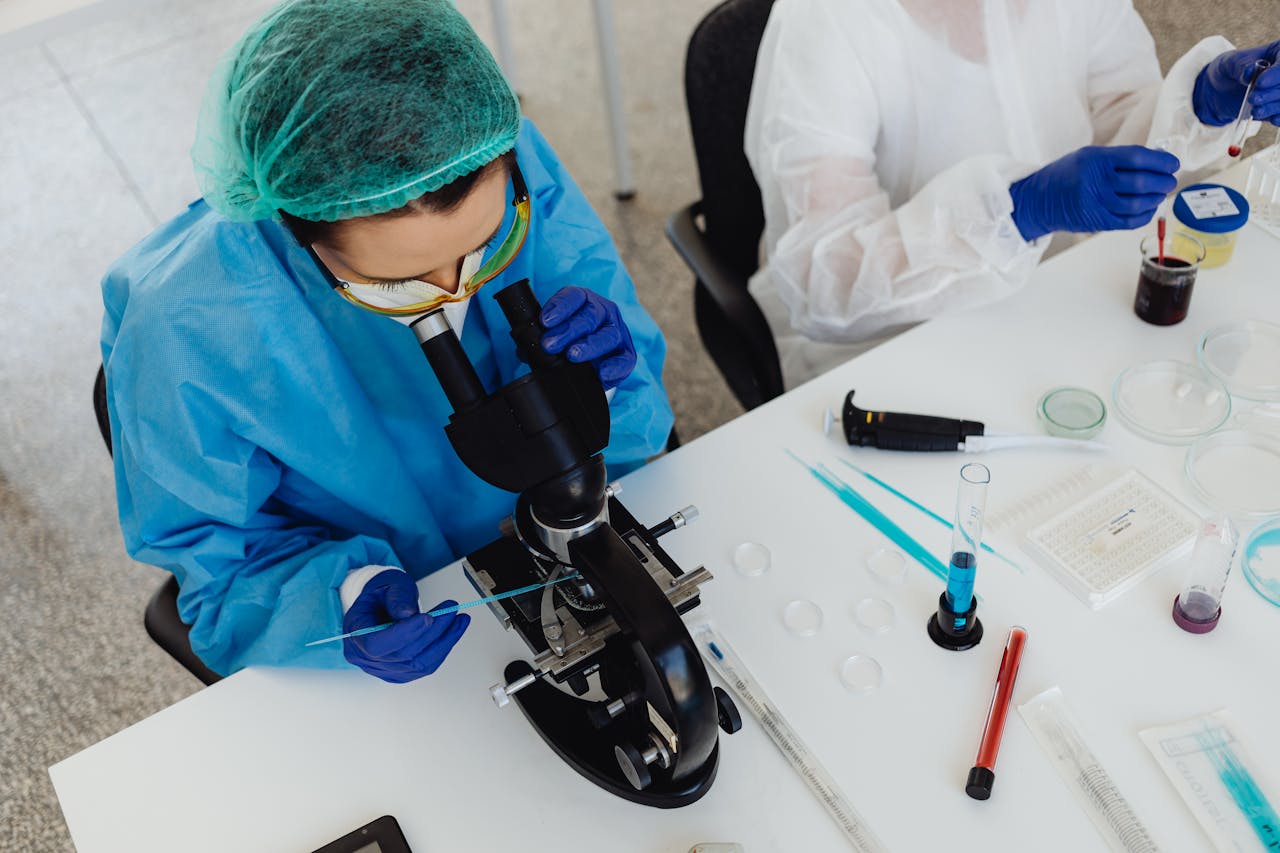 Researchers in PPE examining samples with a microscope in a laboratory setting.